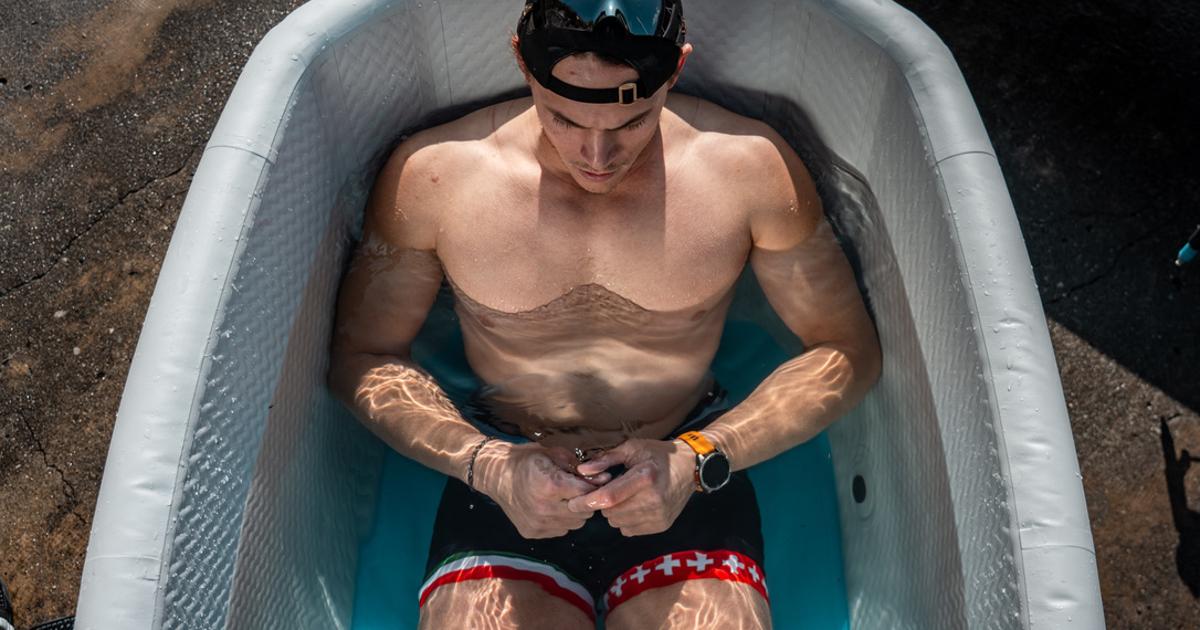 Andrea Panizza sitting in an OBERON Pro ice bath during the Cold Water Challenge, wearing Swiss-themed shorts and a backwards cap, focused and calm under bright sunlight.